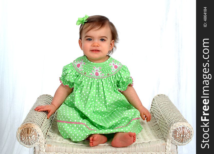 Baby girl in green sitting on bench in front of white background. Baby girl in green sitting on bench in front of white background