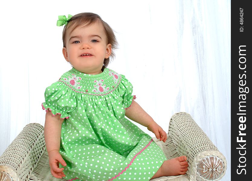 Baby girl in green polka dot dress sitting on bench in front of white background. Baby girl in green polka dot dress sitting on bench in front of white background