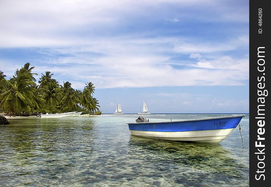 Boat anchored in beautiful tropical cove with palm trees and sailboats in the background. Boat anchored in beautiful tropical cove with palm trees and sailboats in the background.