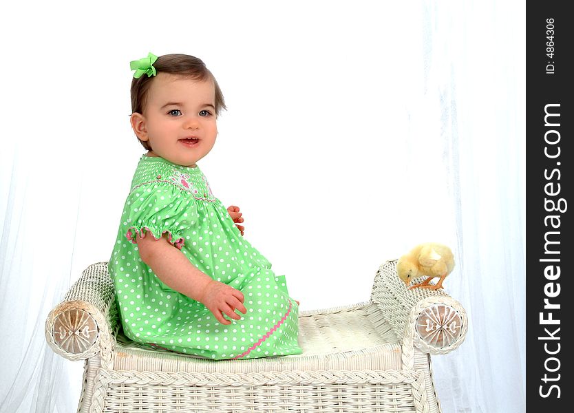 Baby girl on wicker bench looking at camera with chick perched on bench in front of white background. Baby girl on wicker bench looking at camera with chick perched on bench in front of white background