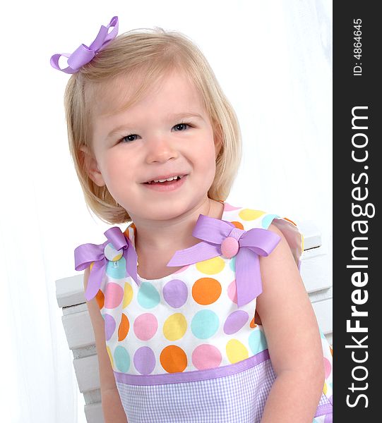 Closeup of smiling blond girl in colorful polka dot dress in front of white background. Closeup of smiling blond girl in colorful polka dot dress in front of white background