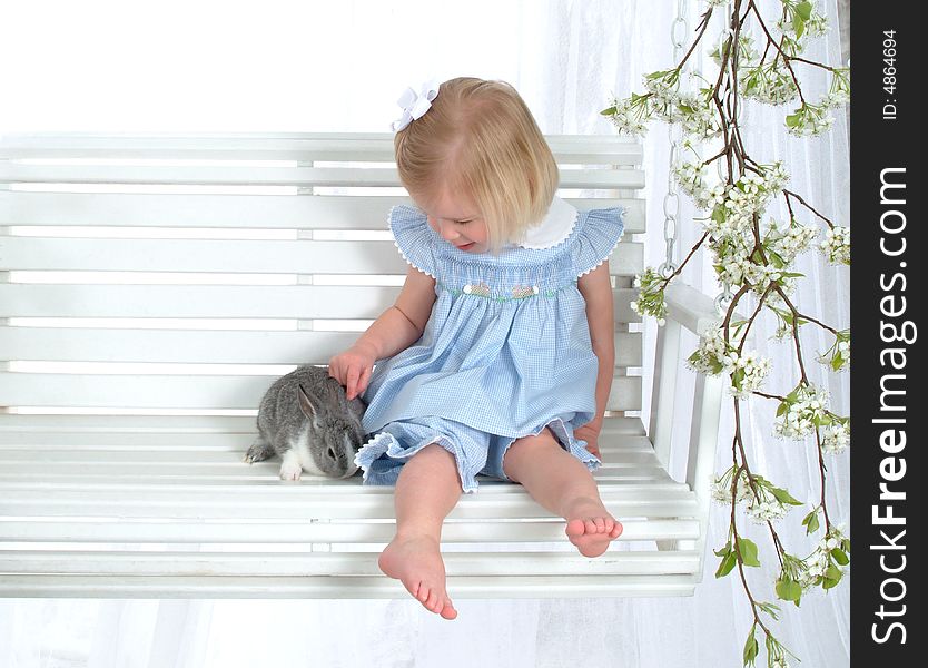 Girl in blue sitting with bunny on swing in front of white background. Girl in blue sitting with bunny on swing in front of white background