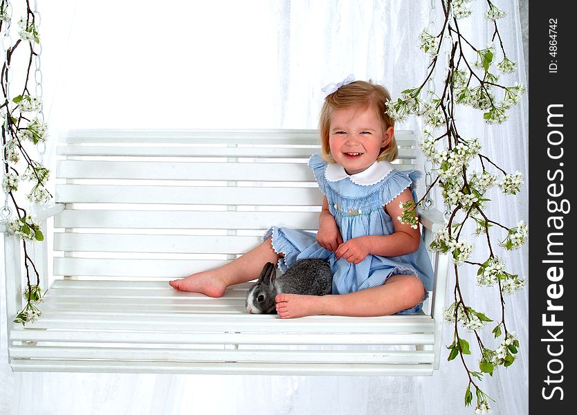 Girl in blue sitting with bunny on swing in front of white background. Girl in blue sitting with bunny on swing in front of white background