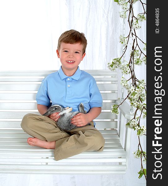 Boy in blue sitting with bunny on swing in front of white background. Boy in blue sitting with bunny on swing in front of white background