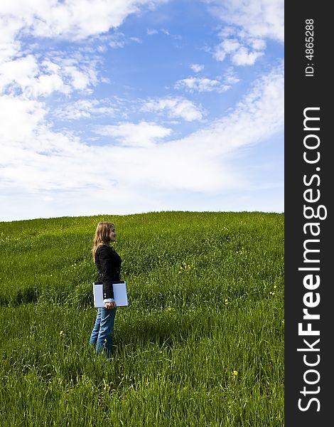 Young woman with laptop in meadow, coy space.