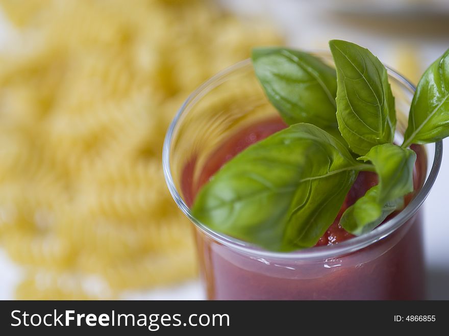 Bowl with tomato sauce and basil and pasta on the background