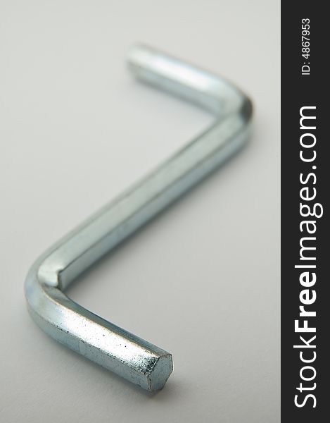 Steel shiny hex key on grey background, distance blur