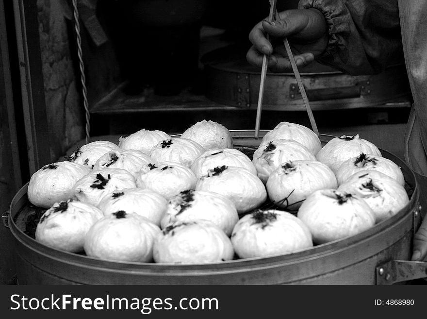 A black and white image of a vendor's hand, holding a pair of chopsticks and using it to get a Chinese steamed bun (called Bao). A black and white image of a vendor's hand, holding a pair of chopsticks and using it to get a Chinese steamed bun (called Bao).