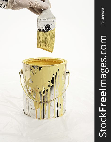 Paint can with yellow drips on the side. Gloved hand dips brush into paint can. Paint can with yellow drips on the side. Gloved hand dips brush into paint can.