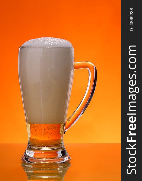 Glass of beer with froth over orange background