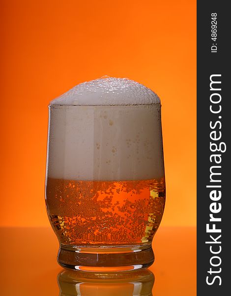 Glass of beer with froth over orange background