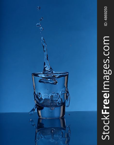 Glass with splashing water over  blue