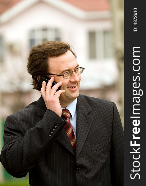 Businessman talking by mobile phone over blurred house background. Businessman talking by mobile phone over blurred house background