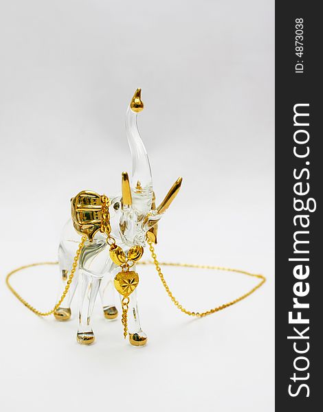 A golden necklace is hanging on the neck of a crystal elephant. A golden necklace is hanging on the neck of a crystal elephant.