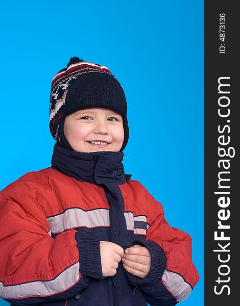 The cheerful boy in a jacket and a cap, on a blue background. The cheerful boy in a jacket and a cap, on a blue background