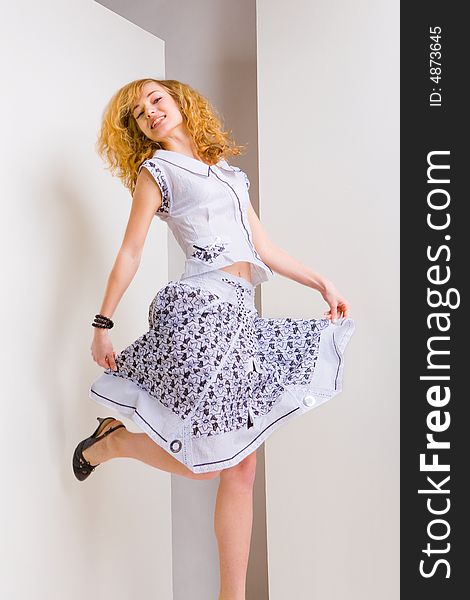 Young woman jumps and fun in the studio. The girl in the bright dress. Laughs. Blonde