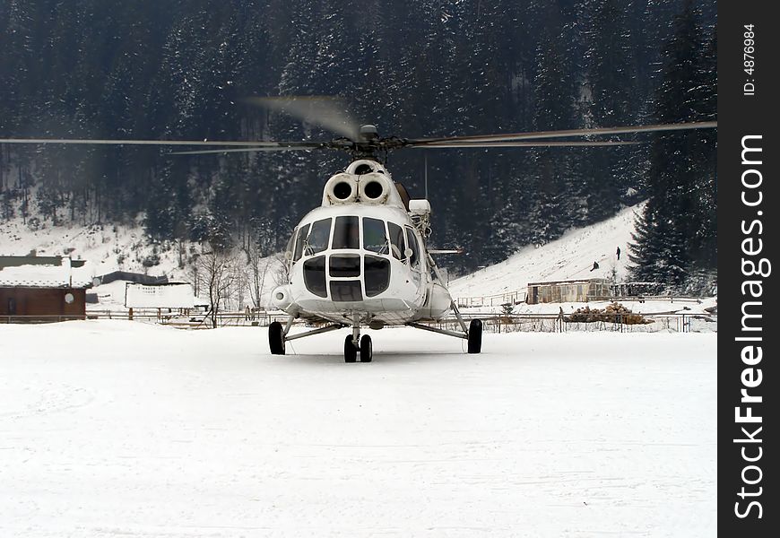 Helicopter landed among the Carpathian mountains, raising snowflakes into air.