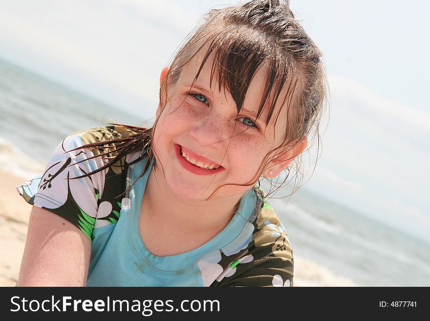A young girl playing on the beach with the ocean behind her.