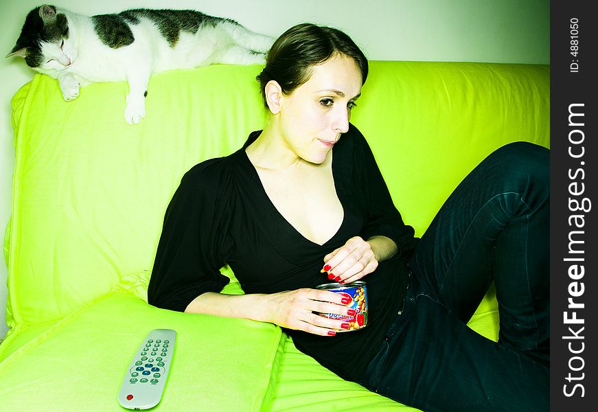 Beautiful girl or young woman with her lazy cat, on sofa, watching TV and eating peanuts. Beautiful girl or young woman with her lazy cat, on sofa, watching TV and eating peanuts