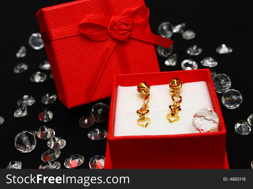 A pair golden earrings in small red box surrounded with crystals.