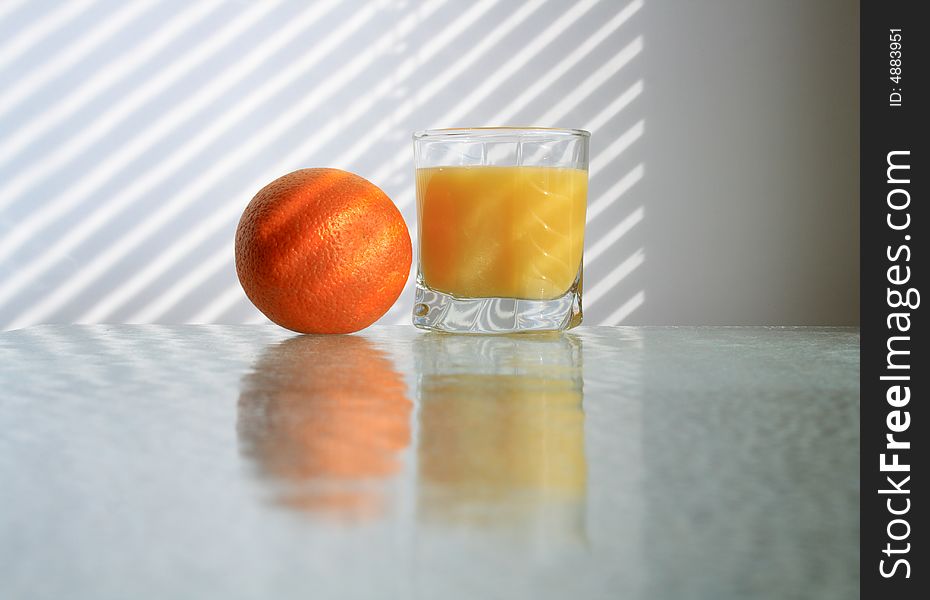 Glass of orange juice and fresh orange on glass table on background with jalousie shadow. Glass of orange juice and fresh orange on glass table on background with jalousie shadow