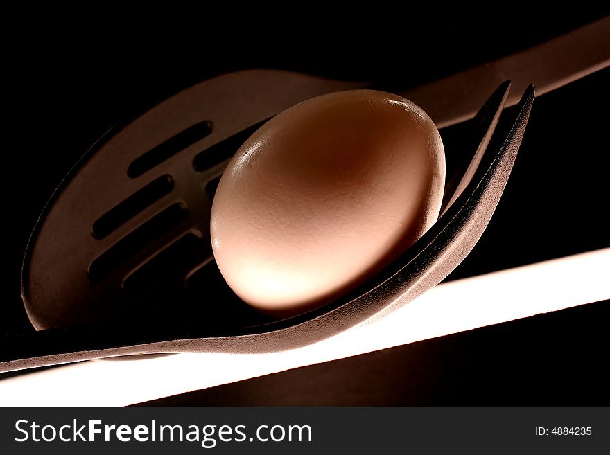 Egg, black spoon with slits,and black plastic fork abstract on black background. Egg, black spoon with slits,and black plastic fork abstract on black background