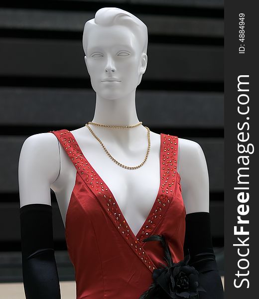 Mannequin dressed in a gown with deep plunging beaded neckline, a black rose ornament, and long velvet gloves, against a black textured wall. Mannequin dressed in a gown with deep plunging beaded neckline, a black rose ornament, and long velvet gloves, against a black textured wall