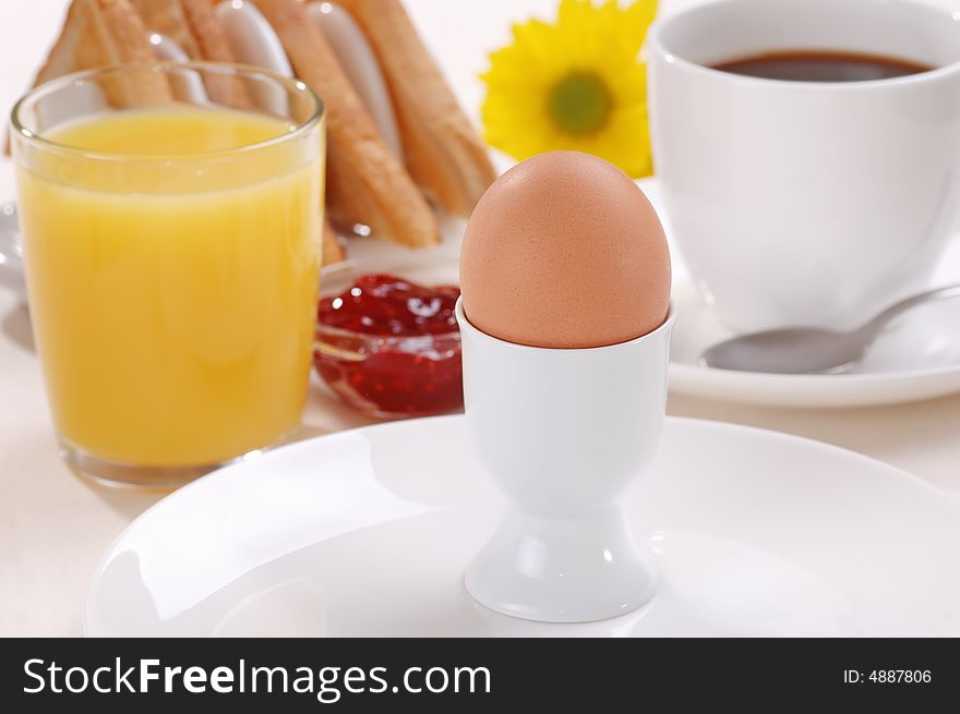 A boiled egg with orange juice, coffee, toast and jam. A yellow flower in the background. A boiled egg with orange juice, coffee, toast and jam. A yellow flower in the background.