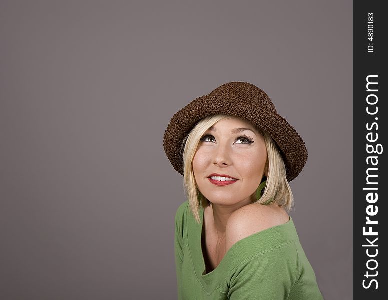 A blonde in a green blouse and a brown hat smiling and looking up. A blonde in a green blouse and a brown hat smiling and looking up