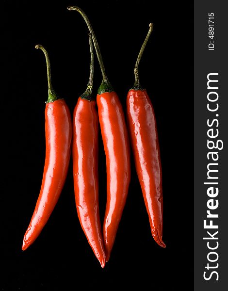 Four isolated red hot chili peppers on the black background. Four isolated red hot chili peppers on the black background