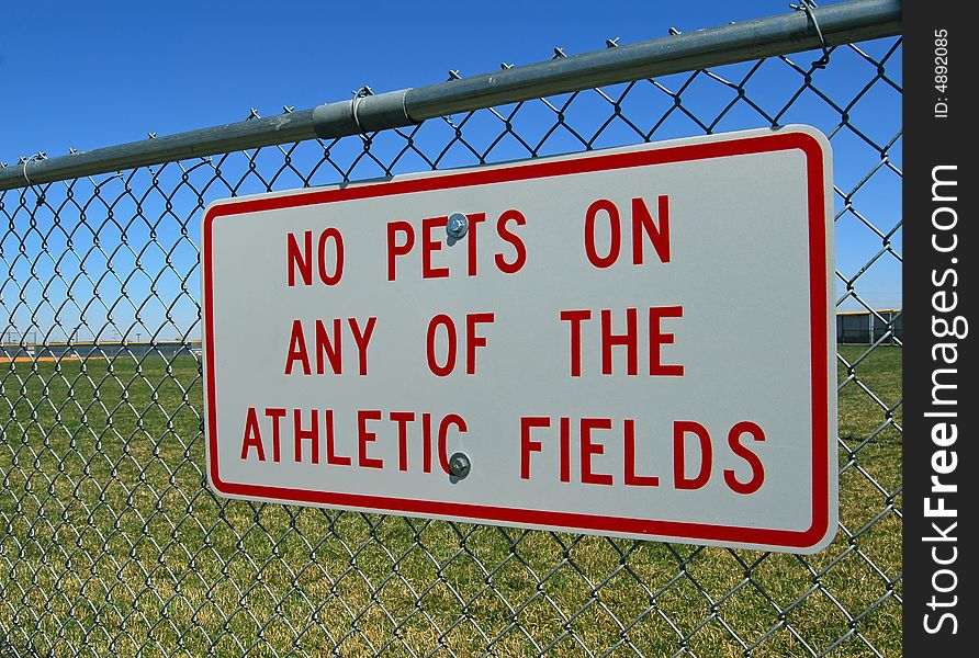 Sign on chain link fence forbidding pets on athletic fields. Sign on chain link fence forbidding pets on athletic fields.