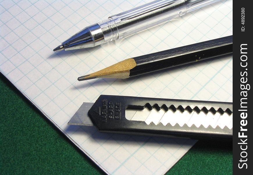 The handle of office, pencil and knife of black color lay on прописи in a cage. The handle of office, pencil and knife of black color lay on прописи in a cage.