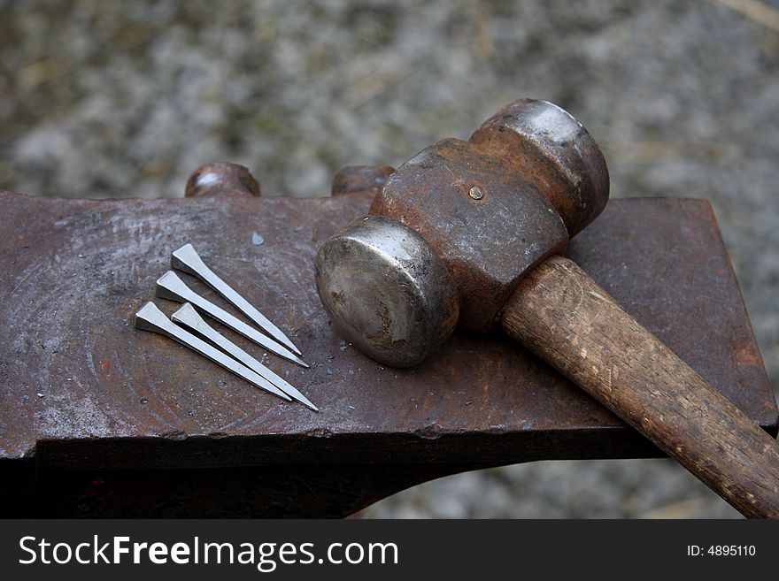 Hammer and horse shoe nails rest on a rusty anvil. Hammer and horse shoe nails rest on a rusty anvil