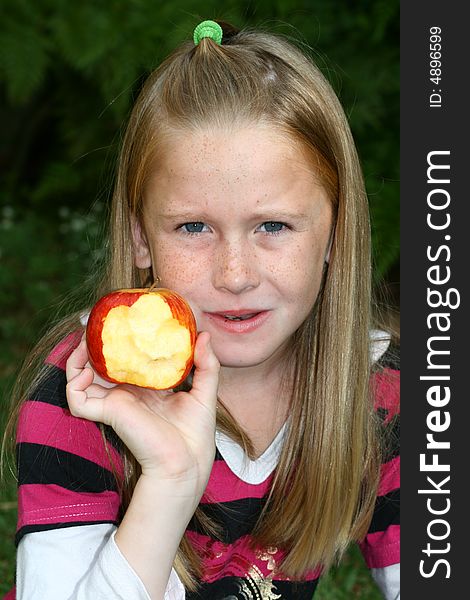 A white caucasian girl child chewing and showing a half eaten apple. A white caucasian girl child chewing and showing a half eaten apple