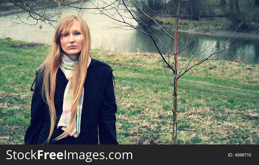 A girl in black with long blond hair standing near the river. A girl in black with long blond hair standing near the river