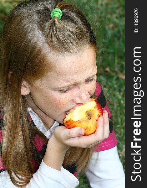 A white caucasian girl child taking a bite of a fresh juicy apple. A white caucasian girl child taking a bite of a fresh juicy apple