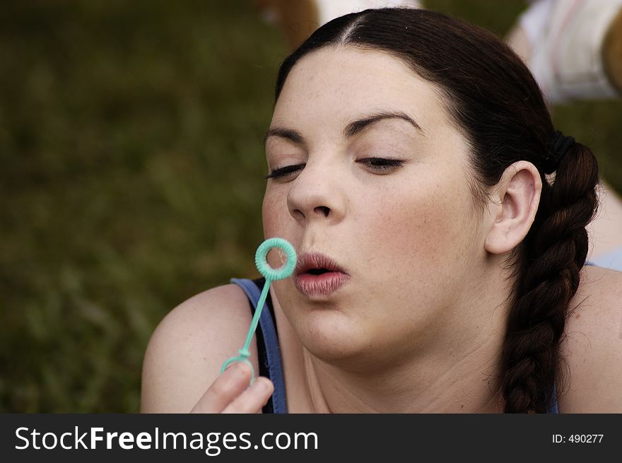 A young female adult relaxes in a park and blows bubbles as she daydreams. A young female adult relaxes in a park and blows bubbles as she daydreams.