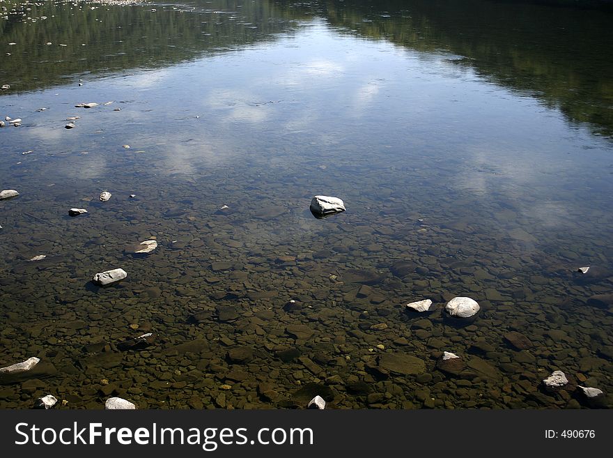 Rocks under the water with cloudy sky reflection