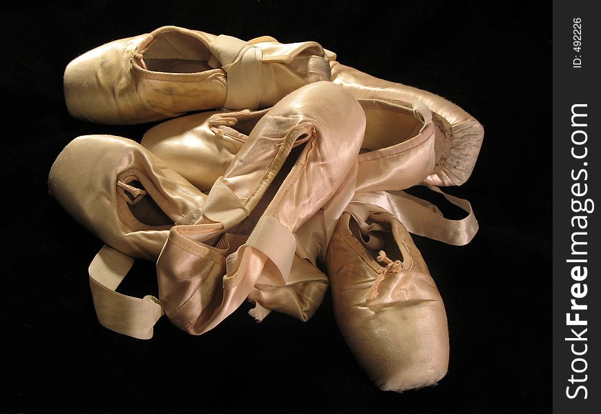 A pile of pink pointe shoes isolated on a black background. A pile of pink pointe shoes isolated on a black background