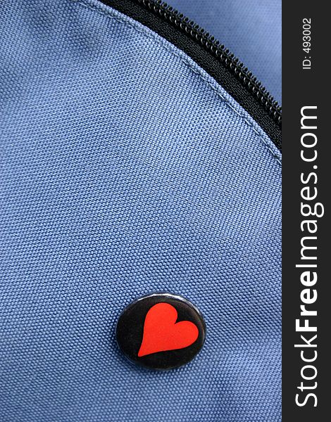 A red heart pin on a jeans-like texture and zip. A red heart pin on a jeans-like texture and zip