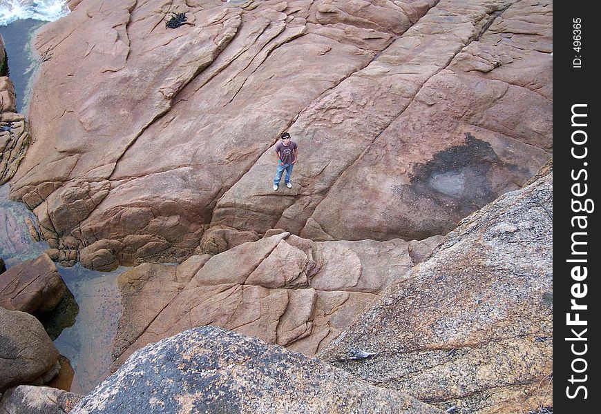 Boy standing on rock platform below cliff. Boy standing on rock platform below cliff
