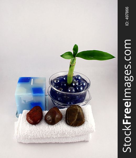 A bamboo shoot in a jar of decorative marbles, a candle, some facecloths and stones