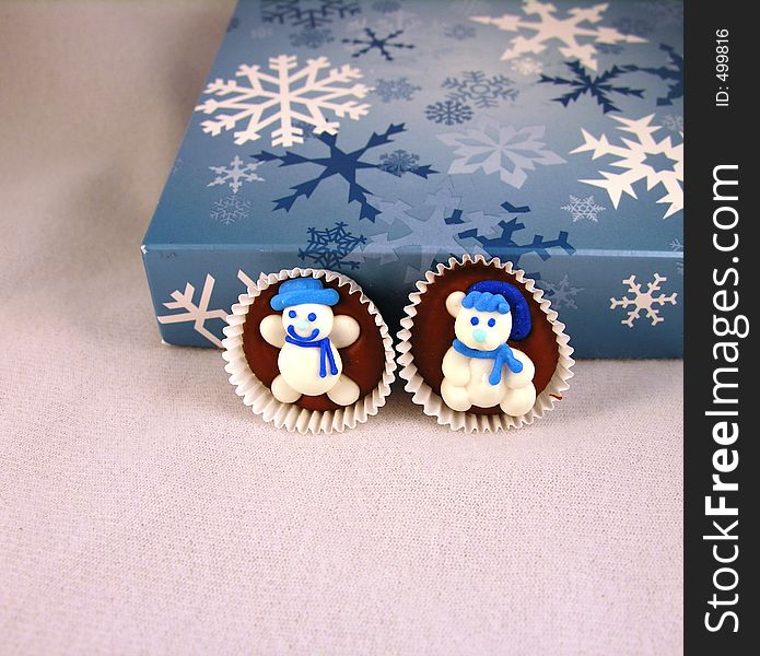 Snowman on chocolate against a box of chocolates, with snowflakes.