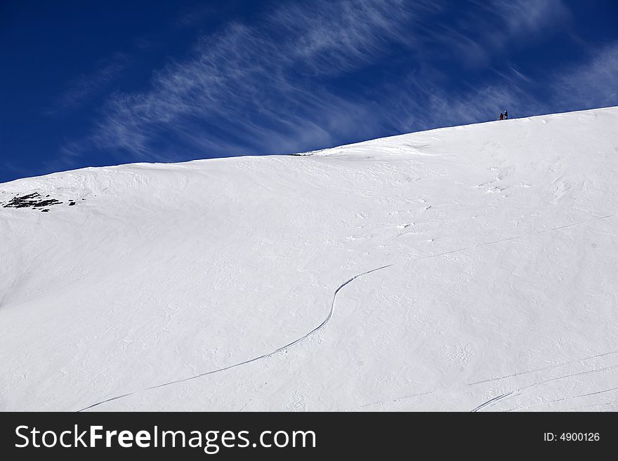 Winter blue sky in high mountains and small skiers