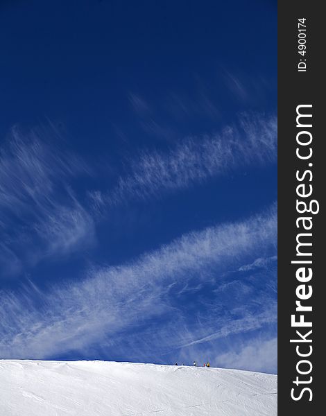 Winter blue sky in high mountains and small skiers