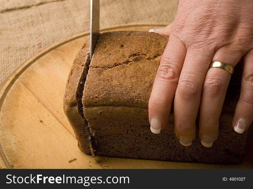 Woman slicing loaf of rye bread on wooden board