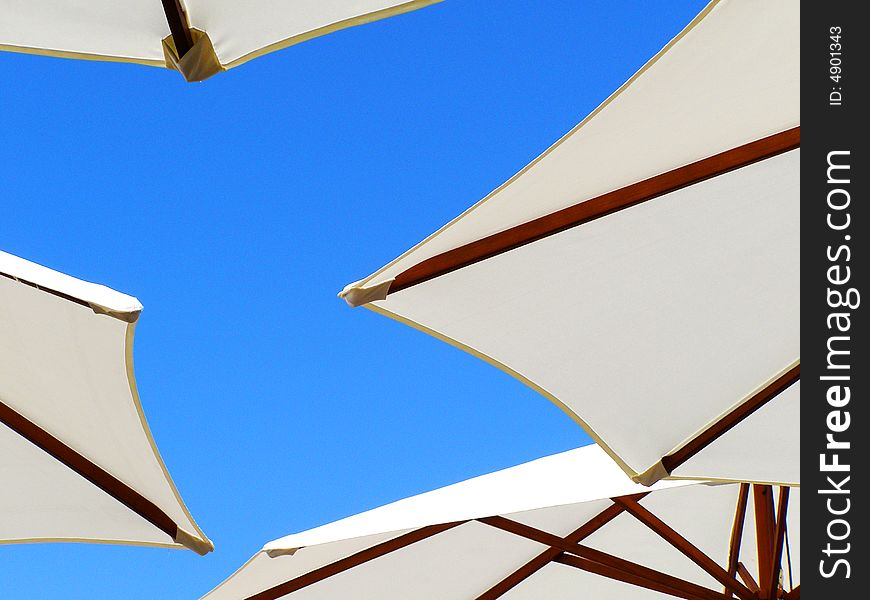 White beach umbrellas with wooden construction under sunny blue sky