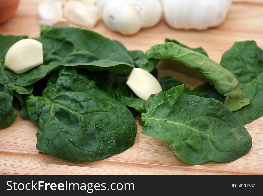 Fresh raw spinach with some garlic on a wodden plate. Fresh raw spinach with some garlic on a wodden plate