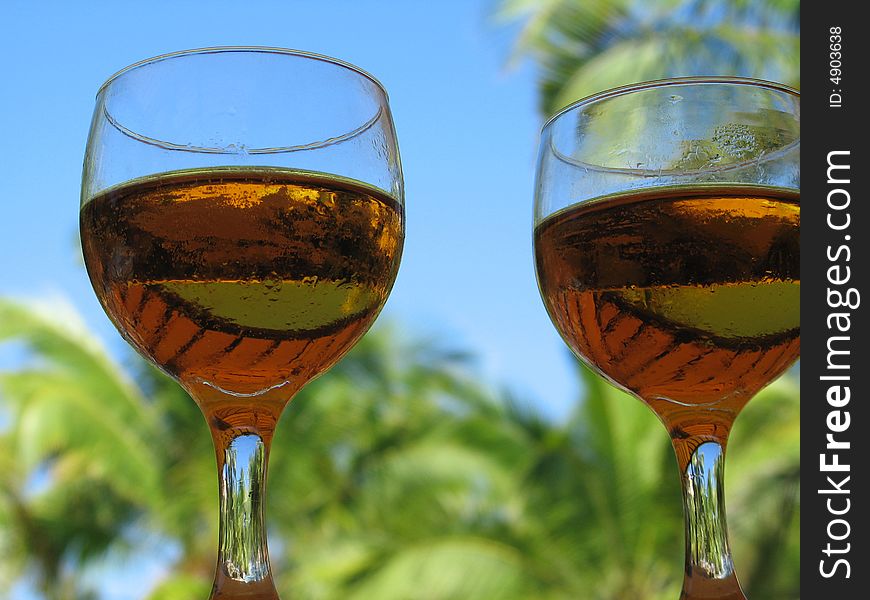 Two beer glasses with sky and palm trees behind