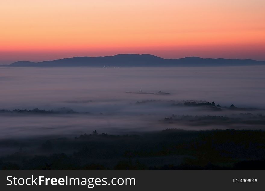 High-wide angle shot of a beautiful dusk scene over the countryside covered in mist. Bela Krajina. Slovenia. High-wide angle shot of a beautiful dusk scene over the countryside covered in mist. Bela Krajina. Slovenia